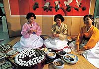 Женщины в национальных костюмах по случаю праздника урожая заняты приготовлением сонпхен, рисовых пирожков